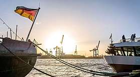 Der Hamburger Hafen bei Sonnenuntergang. Im Vordergrund liegen Schiffe mit Deutschlandfahne.