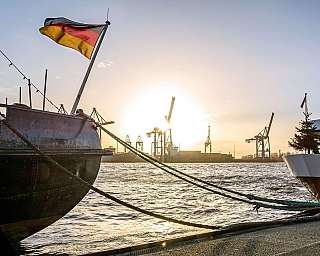 Der Hamburger Hafen bei Sonnenuntergang. Im Vordergrund liegen Schiffe mit Deutschlandfahne.